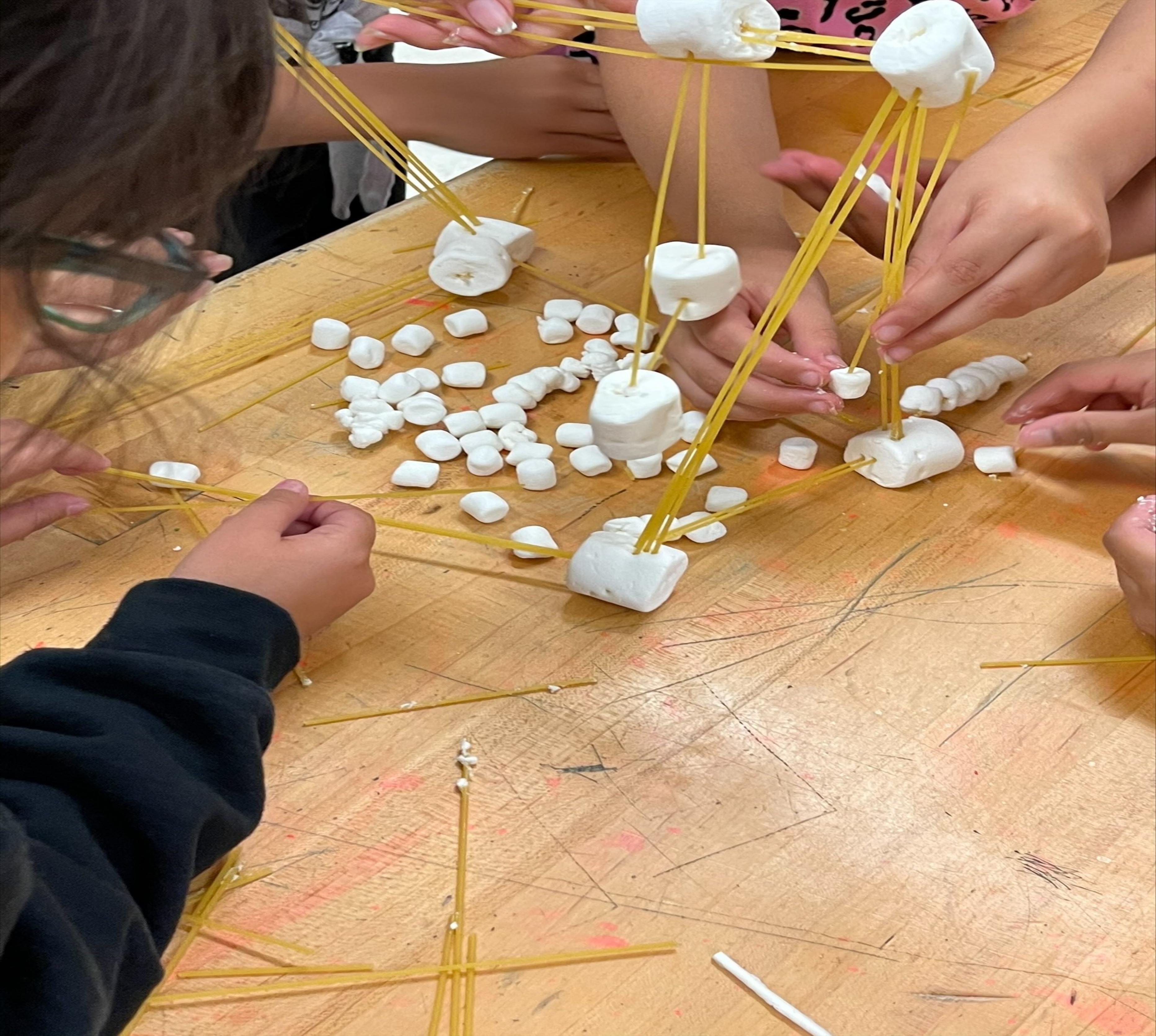 Small group of students working together to build a noodle and marshmallow structure.
