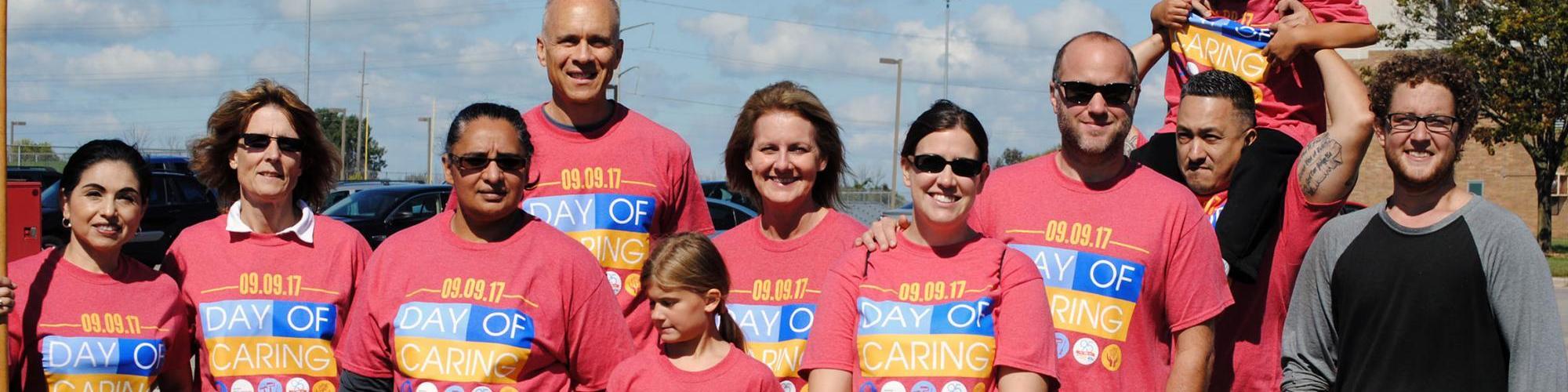 A group of about ten people in Day of Caring shirts stand in a line and smile for the camera.
