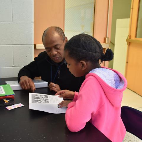 A man tutors a young girl in reading