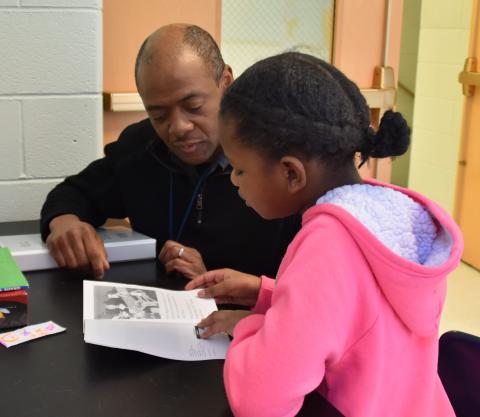A man tutors a young girl in reading.