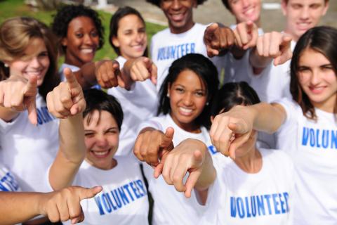 People wearing shirts that say volunteer on them. The people are pointing at the camera.