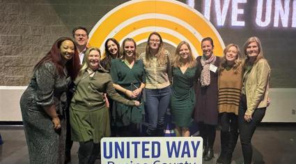 Small group of people gathered behind a sign that says United Way Racine County and in front of a yellow rainbow